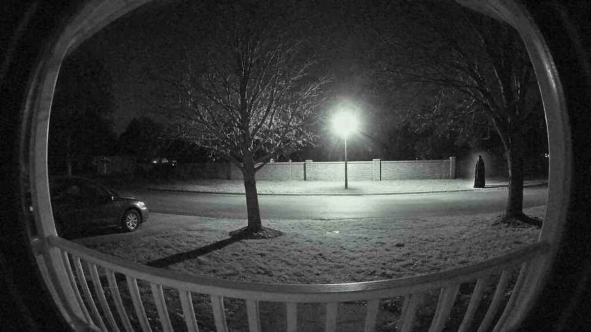 A neighbour's doorbell camera at night: a tall robed figure at the far end of the wall across the street